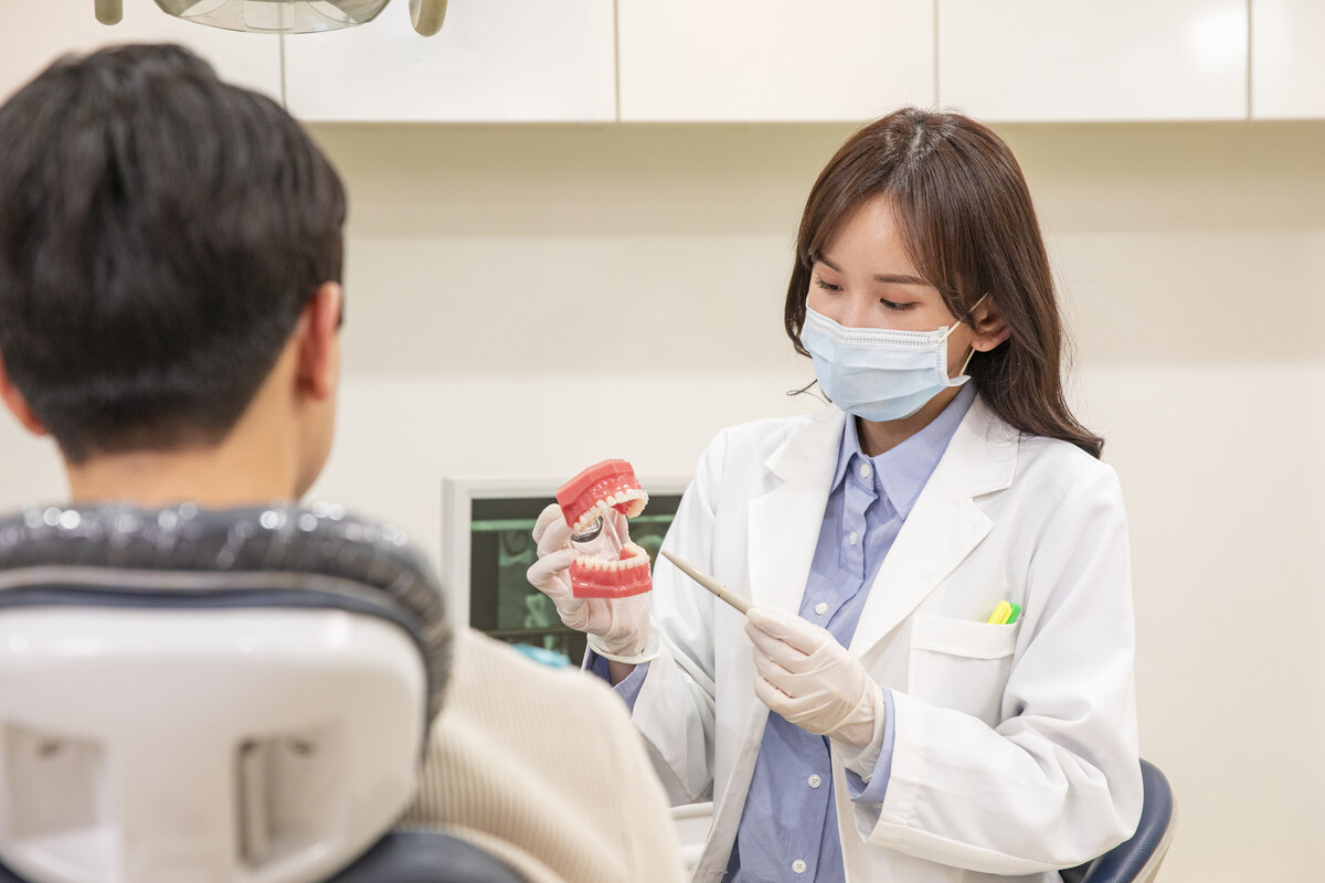 치과 진료 의자에 앉은 환자에게 의료진이 구강 모형으로 치료 계획을 설명하는 모습