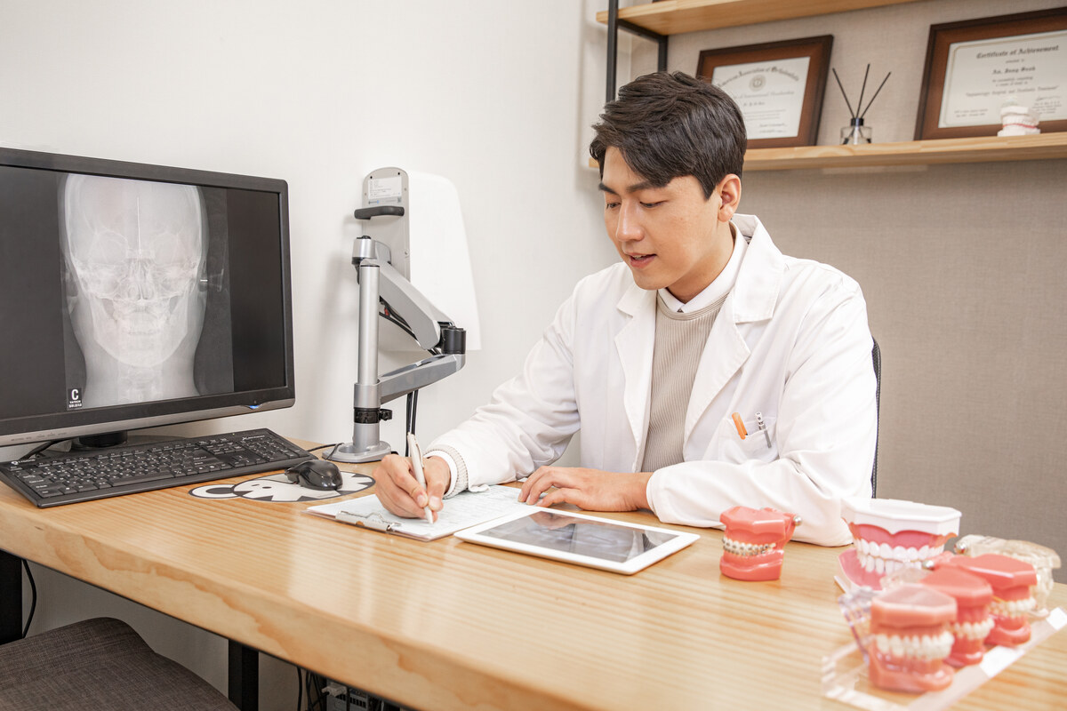 의료진이 엑스레이 화면을 보며 진료 기록을 적고 책상에 구강 모형이 놓인 모습