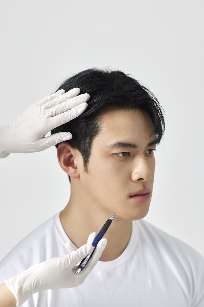 장갑을 낀 의료진이 펜으로 남성 환자의 귀 앞 턱관절 부위를 짚어 확인하는 모습