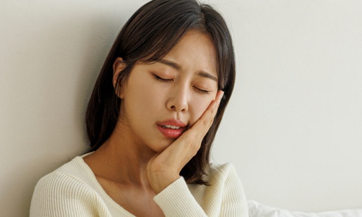 한쪽 턱과 볼을 손으로 감싸고 통증을 느끼는 모습
