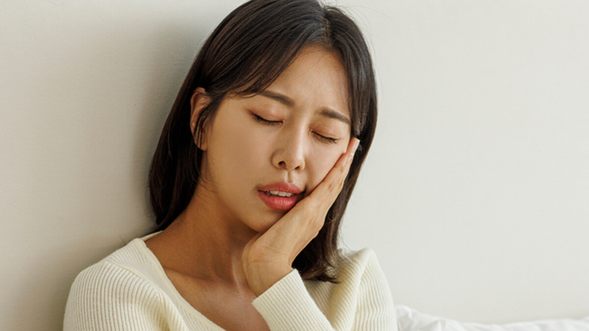 한쪽 턱과 볼을 손으로 감싸고 통증을 느끼는 모습
