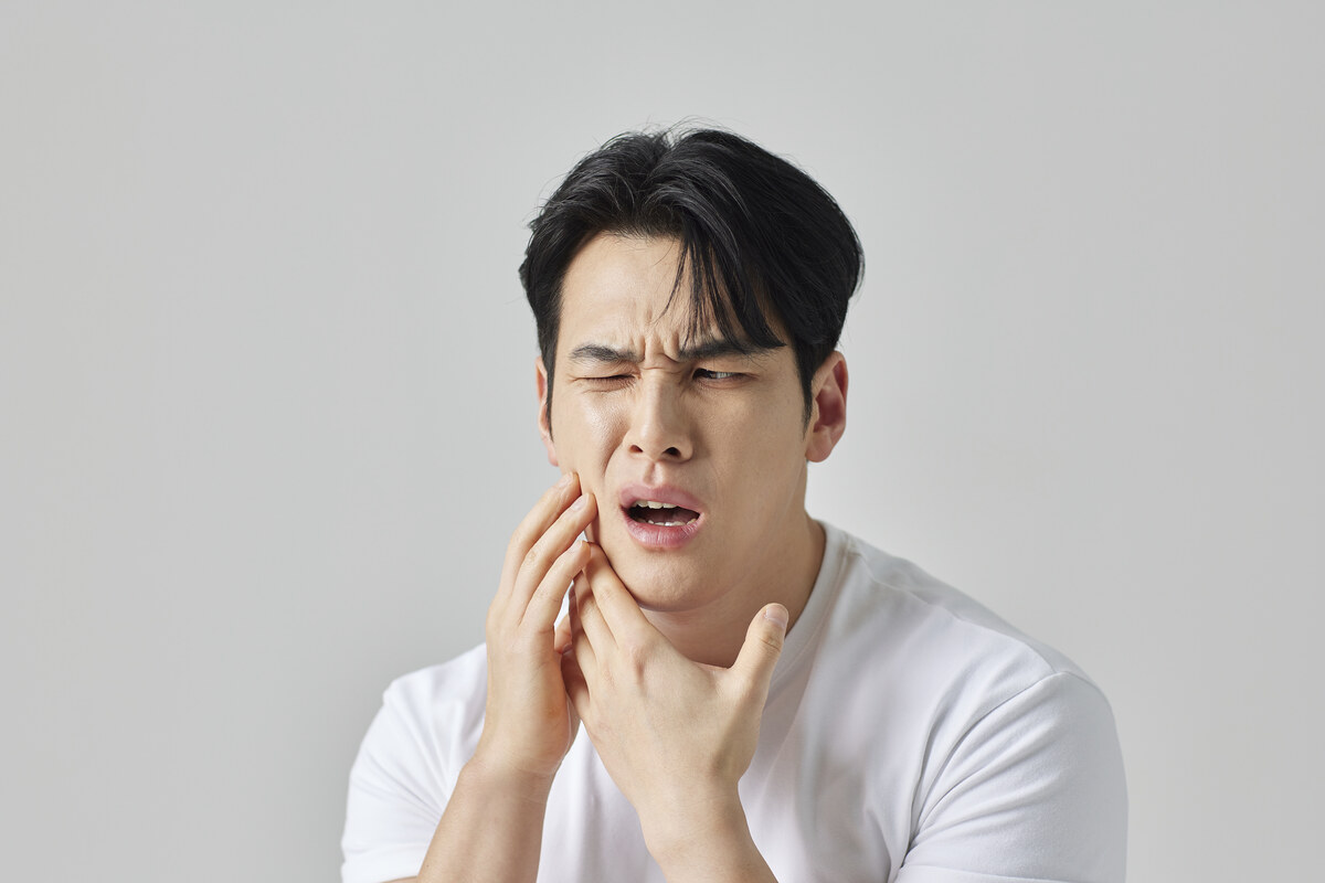 입을 벌릴 때 턱이 아파 양손으로 턱 주변을 감싼 남성